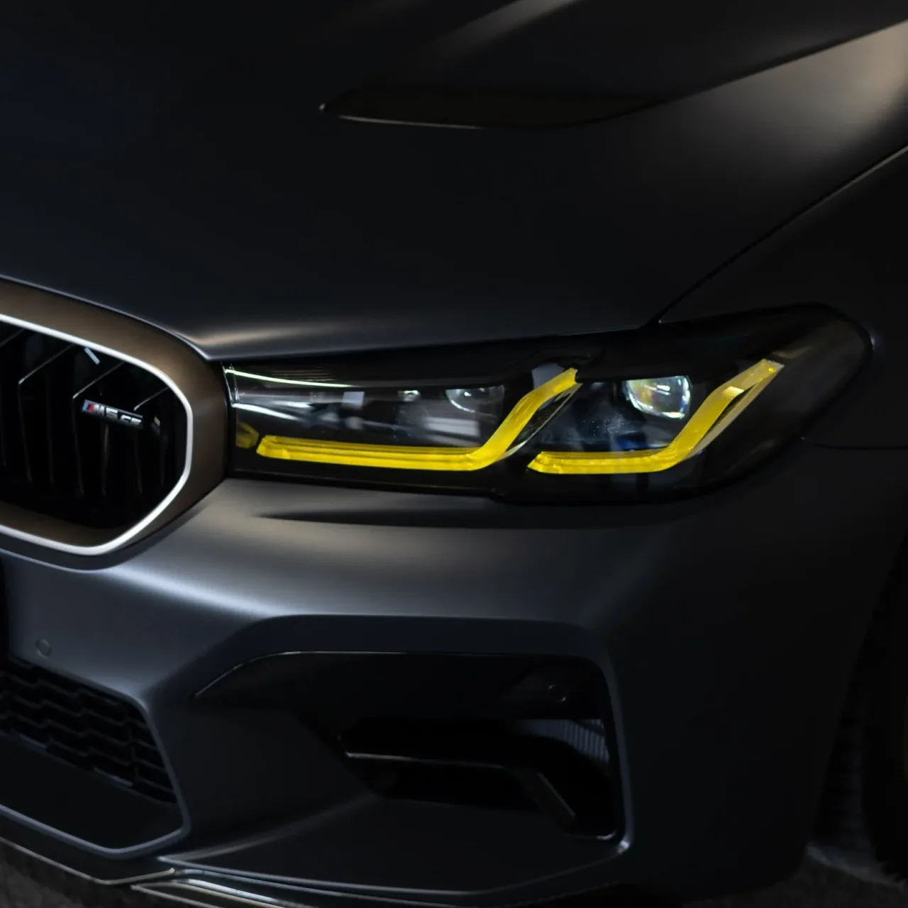 Gele custom dagrijverlichting in de koplamp van een matzwarte BMW M5
