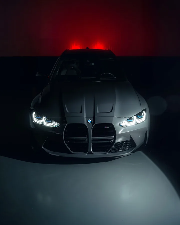 Grijze BMW M3 Touring recht van voren in een donkere studio