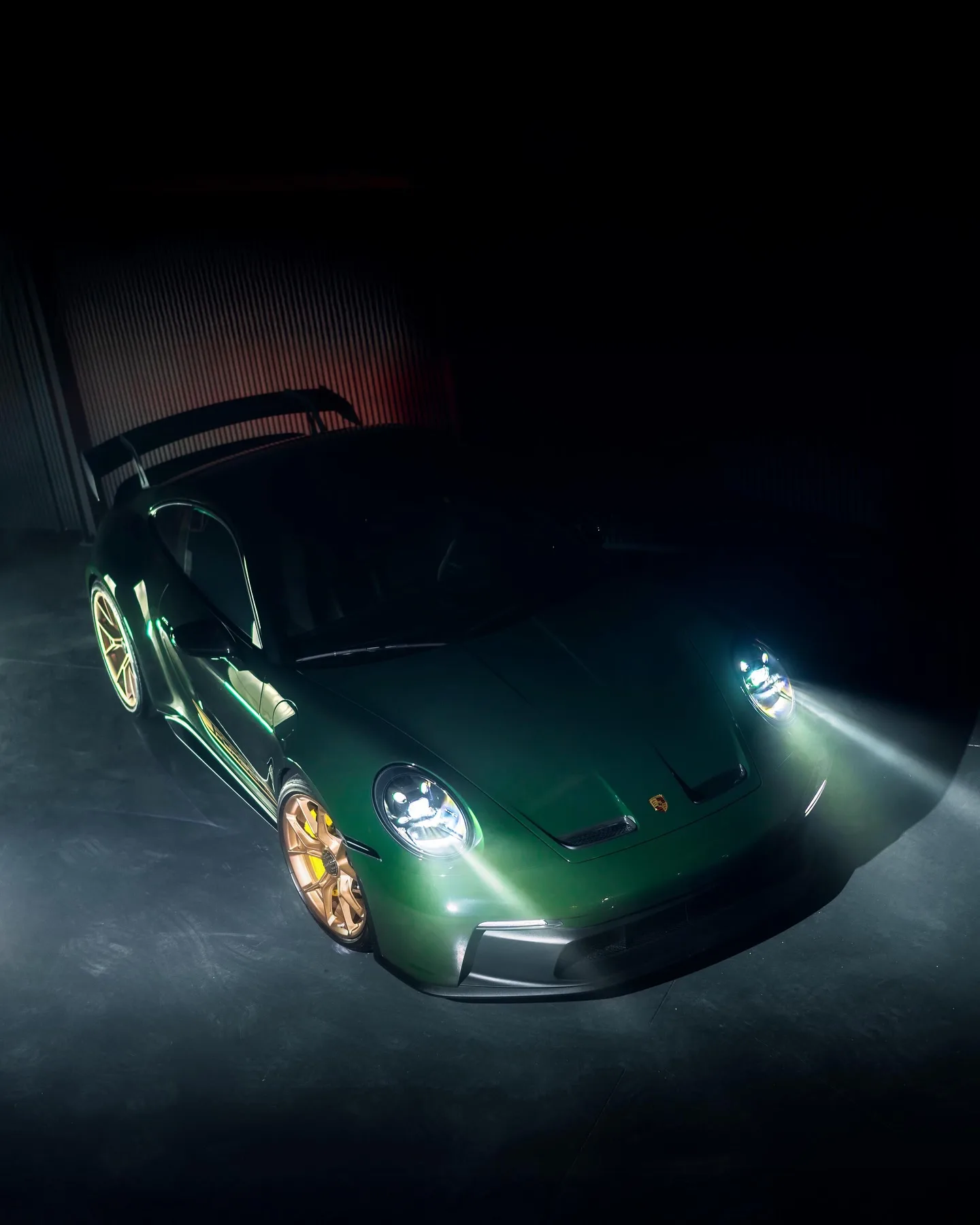 Groene Porsche 992 GT3 schuin van voren van bovenaf, de koplampen aan