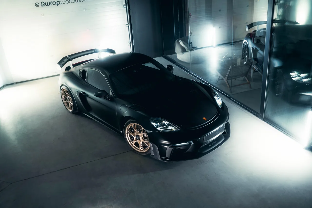 Porsche GT4 RS gewrapt in Satin Black met gouden velgen, schuin van voren in de studio