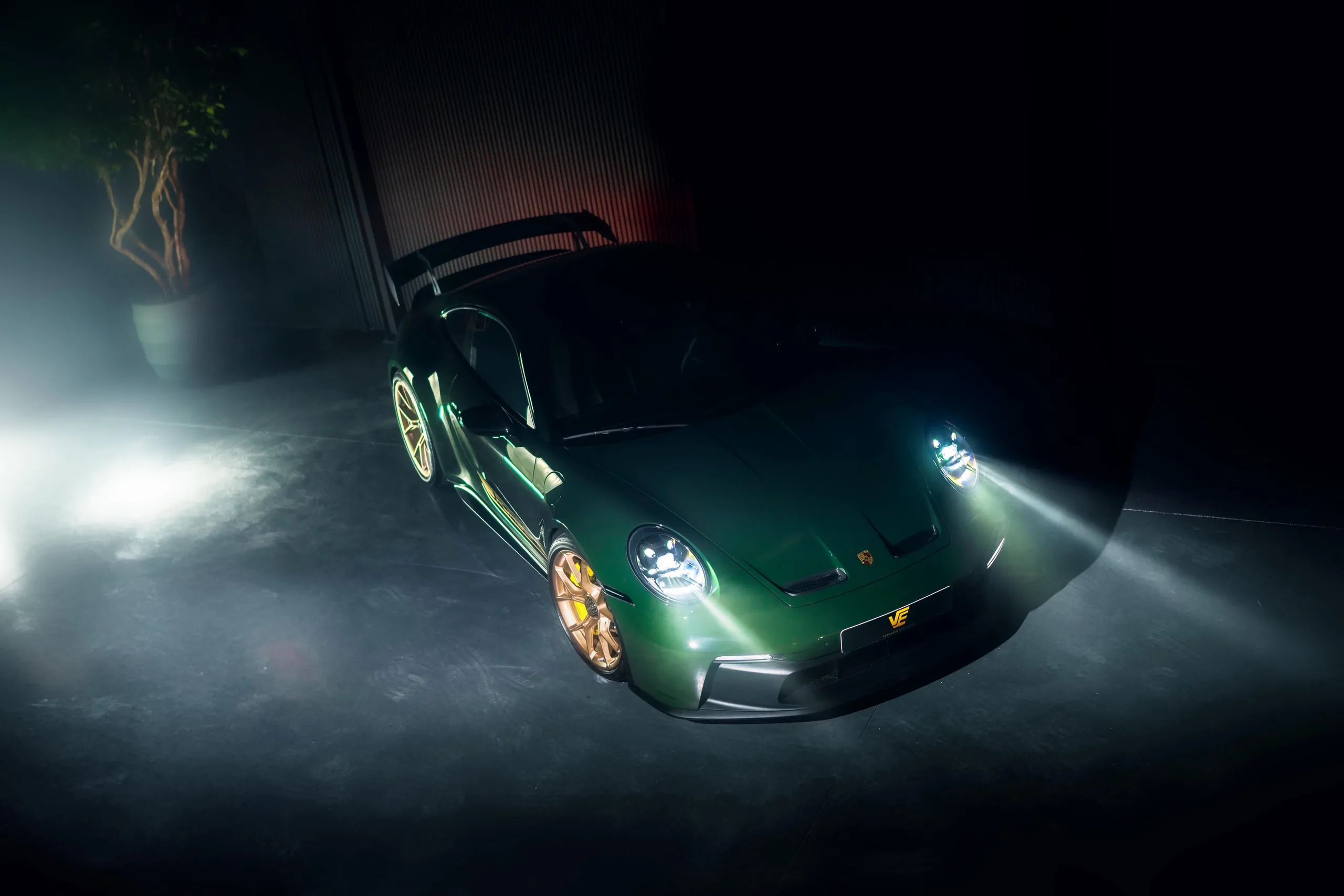 Groene Porsche 992 GT3 met gouden velgen in het donker, de koplampen aan